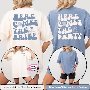 Puede incluir: Dos camisetas de gran tamaño con un diseño retro. Una camiseta es de color marfil con texto azul que dice "Here Comes The Bride" y la otra camiseta es azul con texto marfil que dice "Here Comes The Party".