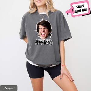 May include: A dark gray t-shirt with a white graphic of a person's face and the text "Add Your Text Here".