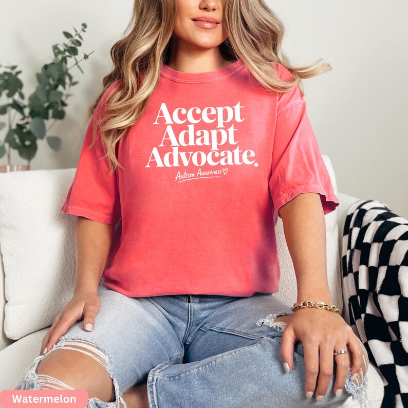 A woman wearing a red t-shirt with the text "Accept Adapt Advocate Autism Awareness" is sitting on a couch.