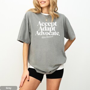 A woman wearing a grey t-shirt with the text "Accept Adapt Advocate" printed on it.