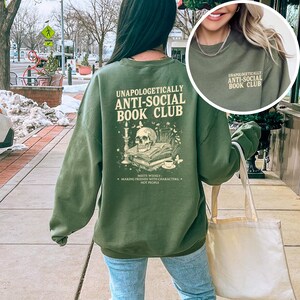 A person wearing a green sweatshirt with text and an illustration on the back is walking on a sidewalk.