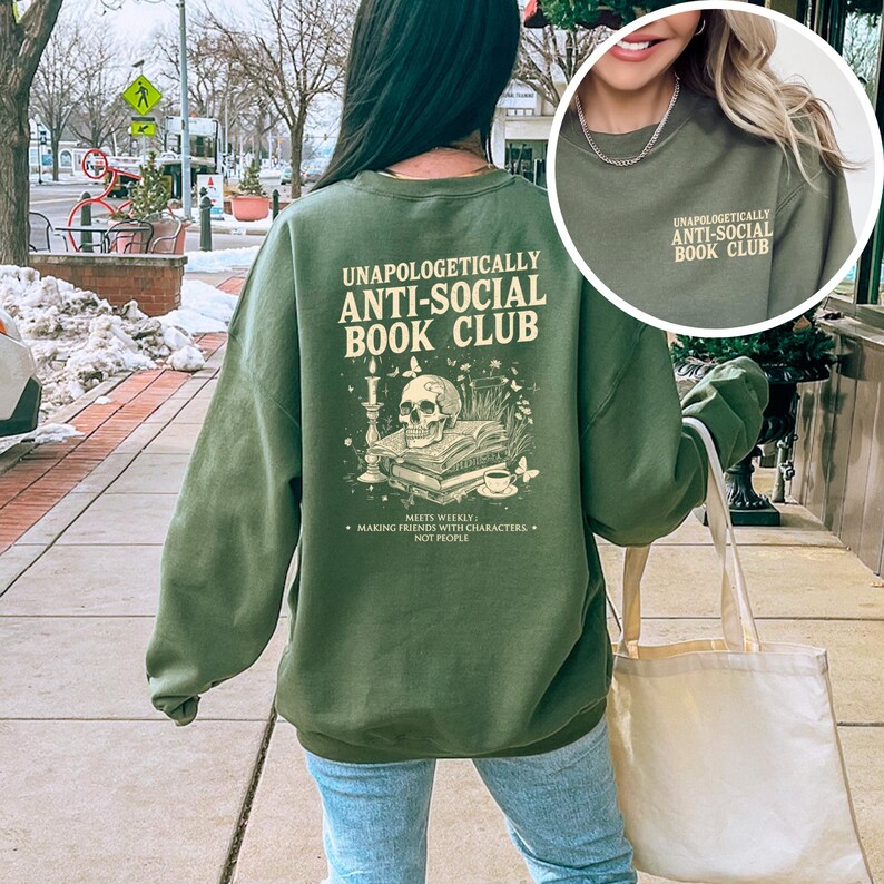 A person wearing a green sweatshirt with text and an illustration on the back is walking on a sidewalk.