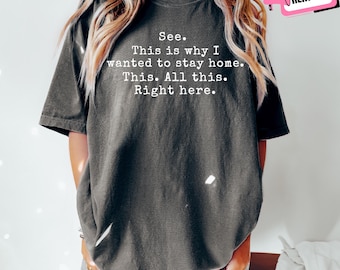 May include: A dark gray t-shirt with the text "See. This is why I wanted to stay home. This. All this. Right here." printed in white. The shirt is a casual style.