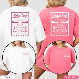 May include: A white and a pink t-shirt featuring a large back graphic of a postage stamp design with a lake, dock, and sun, labeled Lake Crew Lake Travis Johnson Family 2026. The front chest area displays a smaller matching sun and lake graphic.