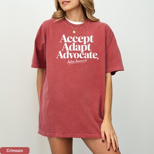 A woman wearing a red t-shirt with the text "Accept Adapt Advocate" printed on it.