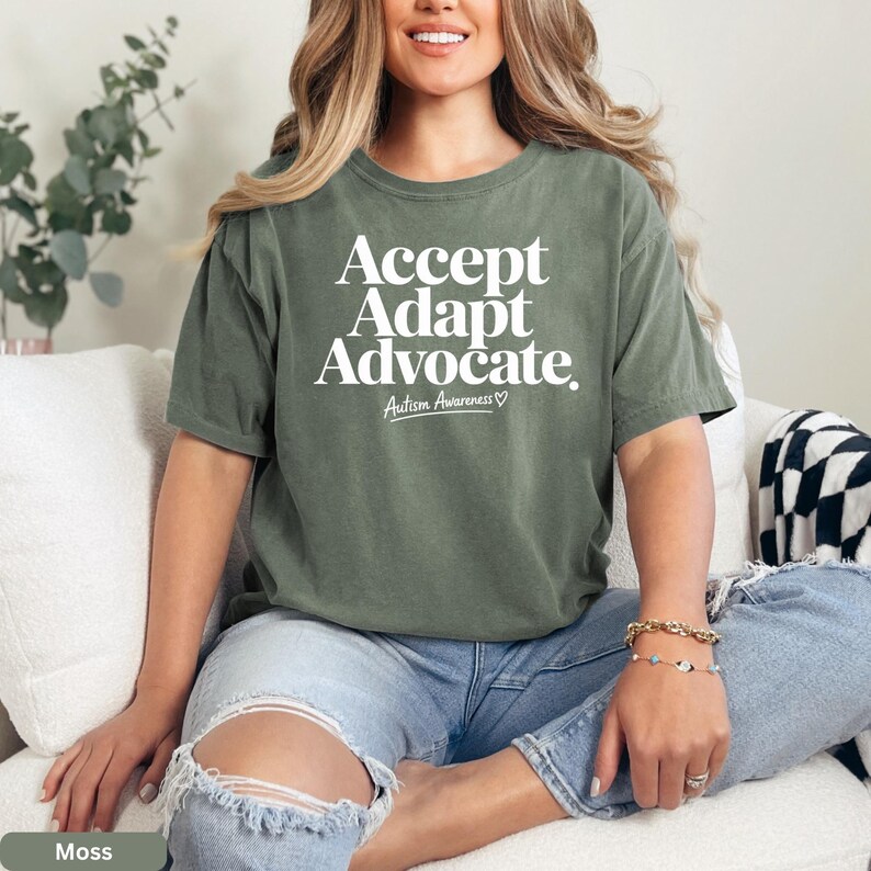 A woman wearing a green t-shirt with the text "Accept Adapt Advocate Autism Awareness" is sitting on a couch.