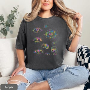 A woman wearing a black t-shirt with a colorful graphic of eyes and a black and white checkered blanket.