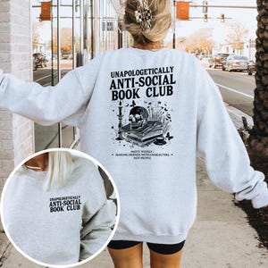 A person wearing a grey sweatshirt with text and graphics printed on the back, standing on a sidewalk with a city street and traffic in the background.