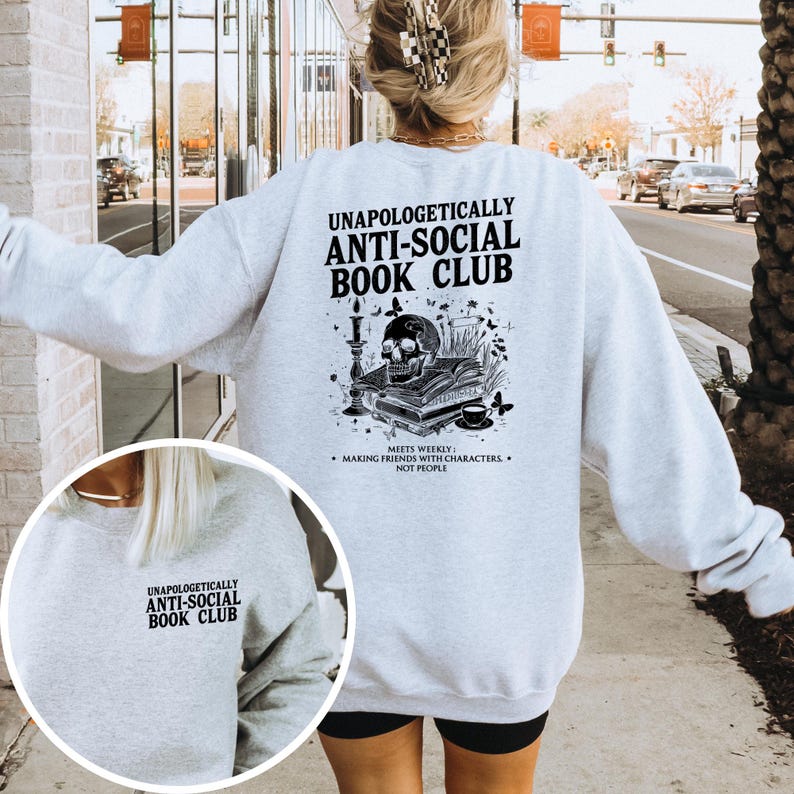 A person wearing a grey sweatshirt with text and graphics printed on the back, standing on a sidewalk with a city street and traffic in the background.