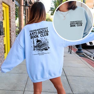A woman wearing a light blue sweatshirt with text printed on the back, standing on a sidewalk.