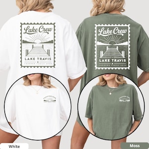 May include: A white and a moss green t-shirt, each featuring a large back graphic of a postage stamp design with a lake, dock, and sun, labeled Lake Crew Lake Travis Johnson Family 2026. The front chest displays a smaller matching sun graphic.