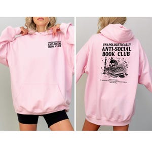 A woman wearing a pink hoodie with text and graphics on the back.