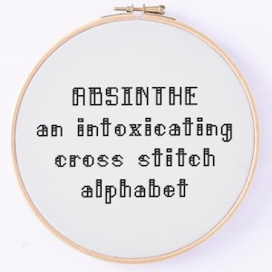 Può includere: Un telaio da ricamo rotondo con le parole "ABSINTHE an intoxicating cross stitch alphabet" ricamate con filo nero su tessuto bianco. Il telaio in legno ha una chiusura in metallo.