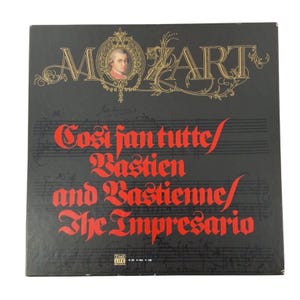 May include: A black vinyl record cover featuring gold lettering that reads MOZART with a portrait of the composer. The text Cosi fan tutte, Bastien and Bastienne, and The Impresario is printed in red. Faint musical notation is visible in the background.