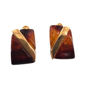 Puede incluir: Un par de pendientes vintage de clip. Cada pendiente presenta una base rectangular con un patrón de carey y un acento diagonal de metal dorado. Los pendientes tienen un acabado pulido y un diseño clásico.