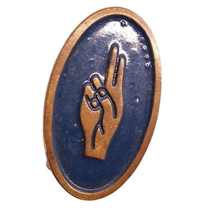 May include: Oval-shaped bronze-colored pin with a blue background. The pin features a hand gesture with the index and middle fingers raised, and the thumb and pinky finger raised. The pin has a bronze-colored border.