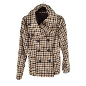 May include: A double-breasted pea coat featuring a brown, black, and cream houndstooth pattern. The coat has a wide fold-over collar, long sleeves, and dark circular buttons arranged in two vertical rows down the front of the garment.