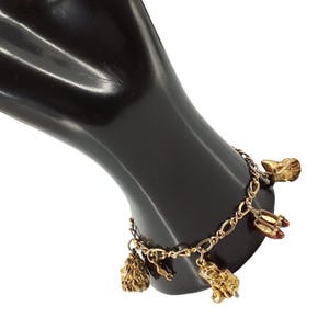 Puede incluir: Una pulsera de dijes de metal en tono dorado con una cadena de eslabones ovalados clásicos. Incluye varios dijes colgantes, entre ellos una cabeza de león texturizada, un par de zapatos pequeños de color rojo y otras figuras metálicas detalladas.
