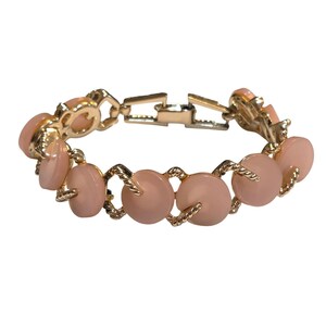 Könnte beinhalten: Ein goldfarbenes Armband mit einer Reihe von runden, rosafarbenen Perlen. Die Perlen sind durch gedrehte, goldfarbene Glieder verbunden. Das Armband hat einen Verschluss.
