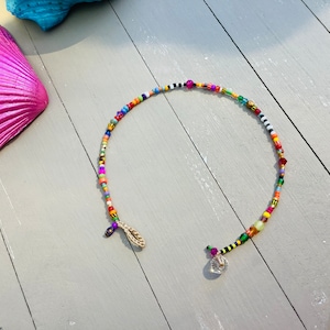 Peut inclure: Un collier de perles colorées avec un pendentif en cristal. Le collier est composé de petites perles colorées, notamment rouge, orange, jaune, vert, bleu, violet et noir. Le collier est enfilé sur un cordon transparent et possède un fermoir simple.