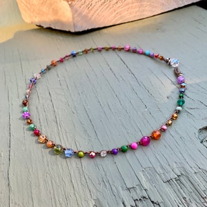 May include: A colourful beaded necklace with a variety of gemstone beads and a brown cord.