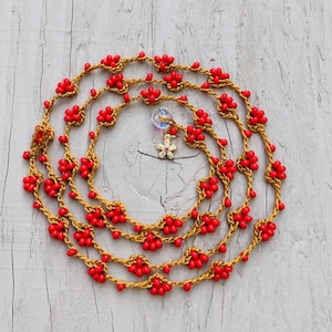 May include: A red and gold beaded necklace with a flower charm. The necklace is made of crocheted cord and features small red beads in the shape of flowers.