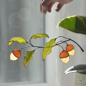 May include: A stained glass acorn branch with green leaves and orange and white acorns hanging from a string.