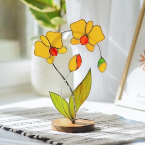 May include: A stained glass orchid flower sculpture with yellow, red, and green glass pieces. The sculpture is on a wooden base.
