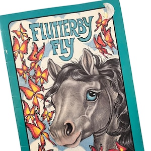Pode incluir: Um livro infantil vintage intitulado "Flutterby Fly". A capa apresenta um cavalo cinzento com olhos azuis, rodeado por borboletas laranja e amarelas. O título está em uma fonte turquesa, com os nomes do autor e do ilustrador abaixo.