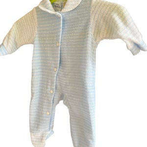 Może przedstawiać: Niemowlęcy pajacyk z frotte w niebiesko-białe paski, z kołnierzykiem i długimi rękawami. Pajacyk ma zapinany na guziki prz&oacute;d i dołączone st&oacute;pki. Ubranko wisi na zielonym wieszaku.