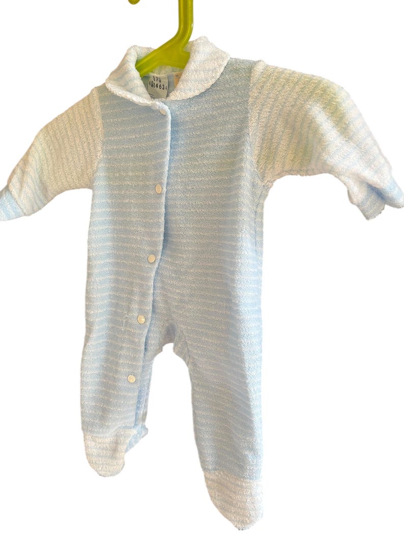 Może przedstawiać: Niemowlęcy pajacyk z frotte w niebiesko-białe paski, z kołnierzykiem i długimi rękawami. Pajacyk ma zapinany na guziki prz&oacute;d i dołączone st&oacute;pki. Ubranko wisi na zielonym wieszaku.