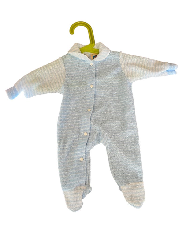 Może przedstawiać: Jasnoniebieski pajacyk dla dziecka z kołnierzykiem i długimi rękawami, zawieszony na zielonym wieszaku. Pajacyk ma zapinany na guziki prz&oacute;d i st&oacute;pki. Tkanina ma wz&oacute;r w paski.