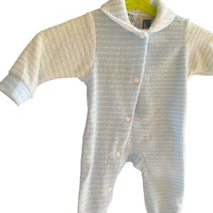 Może przedstawiać: Niemowlęcy pajacyk w niebiesko-białe paski, z kołnierzykiem i długimi rękawami. Pajacyk ma białe guziki i wisi na ż&oacute;łtym wieszaku. Tkanina wydaje się być miękkim frotte. Idealny dla niemowląt.