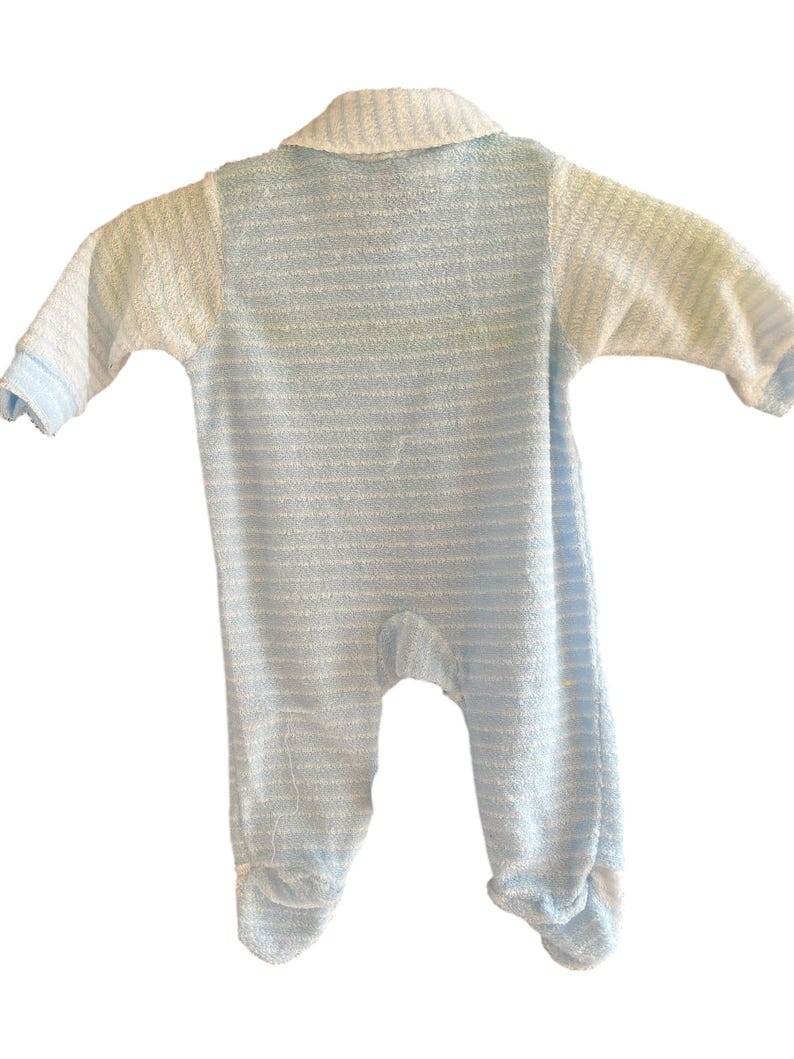 Może przedstawiać: Niemowlęcy pajacyk w niebiesko-białe paski, z długimi rękawami i zintegrowanymi st&oacute;pkami. Pajacyk ma kołnierzyk i jest wykonany z miękkiej, teksturowanej tkaniny. Klasyczny design, odpowiedni dla noworodk&oacute;w.