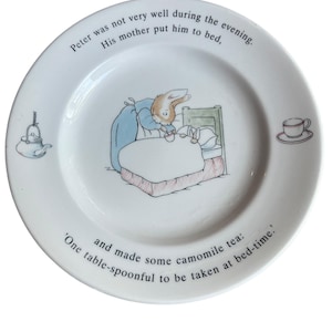 May include: A white ceramic plate with a blue and white illustration of Peter Rabbit in bed. The plate has text that reads: "Peter was not very well during the evening. His mother put him to bed. 'One table-spoonful to be taken at bed-time.' and made some camomile tea:"