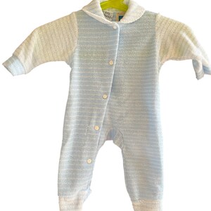 Może przedstawiać: Niemowlęcy śpioszek w jasnoniebieskie i białe paski, z białym kołnierzykiem i rękawami. Śpioszek ma zapinany na guziki prz&oacute;d i wisi na zielonym wieszaku.