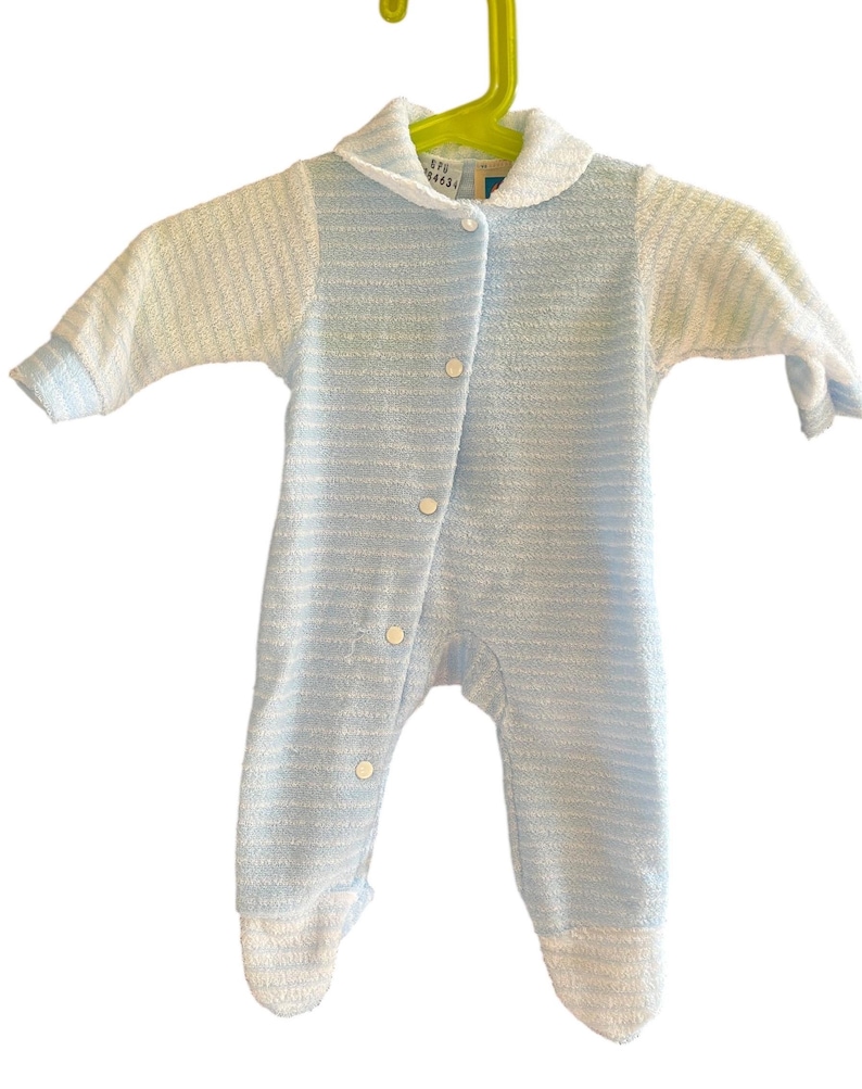 Może przedstawiać: Niemowlęcy śpioszek w jasnoniebieskie i białe paski, z białym kołnierzykiem i rękawami. Śpioszek ma zapinany na guziki prz&oacute;d i wisi na zielonym wieszaku.