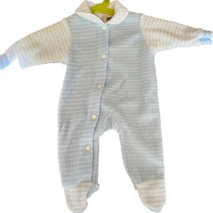 Może przedstawiać: Jasnoniebieski pajacyk dla dziecka z białym kołnierzem i mankietami, zawieszony na zielonym wieszaku. Pajacyk ma zapięcie na guziki z przodu i wz&oacute;r w paski. Materiał wydaje się miękki i teksturowany.