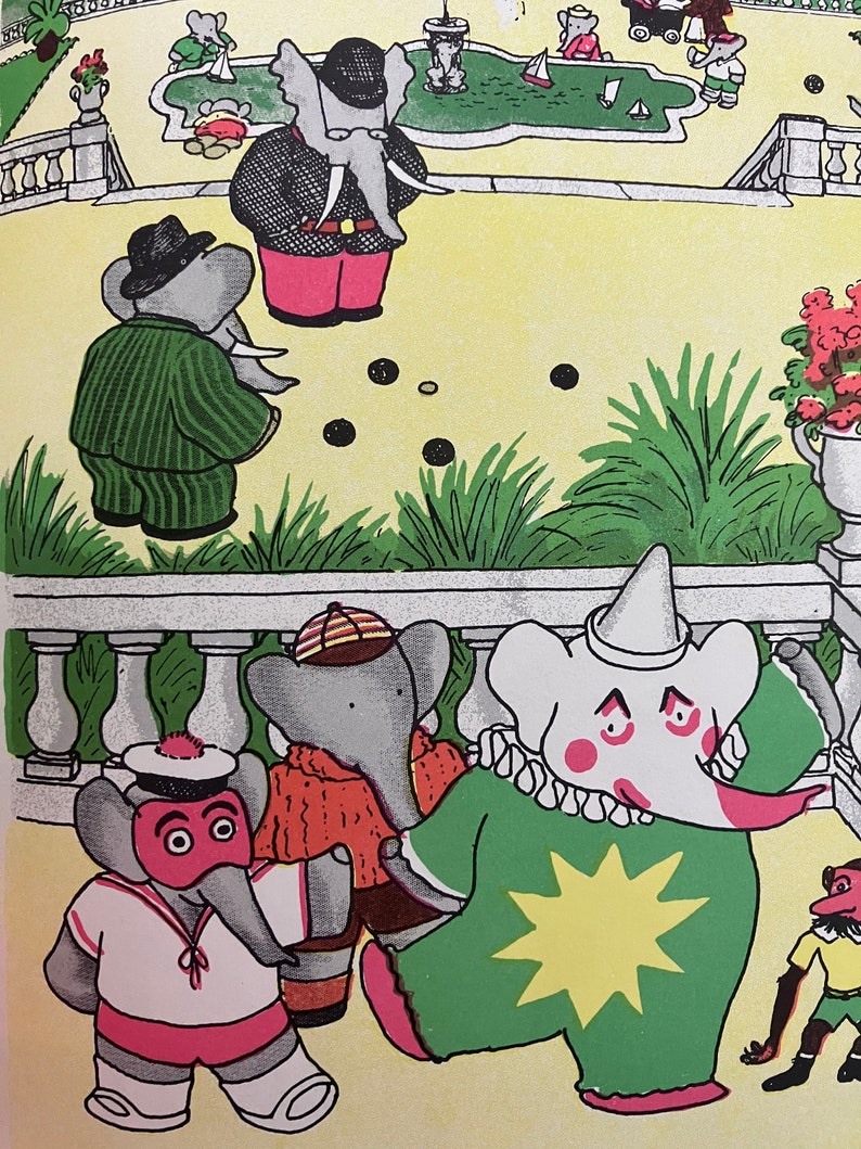 May include: A group of grey elephants wearing different costumes are playing a game of marbles in a garden setting. One elephant is wearing a clown costume with a green and yellow star on the front. Another elephant is wearing a sailor costume with a red and white striped shirt and a red hat. A third elephant is wearing a red and orange jumper and a brown hat. The elephants are playing on a yellow surface with green grass and a white fence in the background.