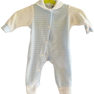 Może przedstawiać: Niemowlęcy pajacyk w niebiesko-białe paski z kołnierzykiem i zapięciem na guziki. Długi rękaw ma stopy i wisi na zielonym wieszaku. Pajacyk wykonany jest z miękkiej, teksturowanej tkaniny.