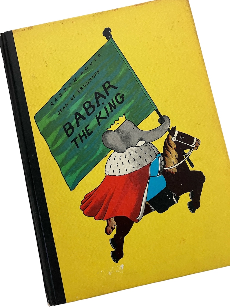 May include: A yellow book cover with a green flag that says "Babar the King" and features a cartoon elephant riding a horse. The book is titled "Babar the King" and is published by Random House, Jean de Brunhoff.