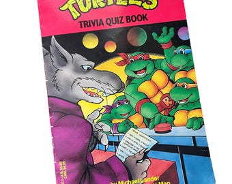 Puede incluir: Un libro de preguntas y respuestas de las Tortugas Ninja Adolescentes con una portada que presenta a las cuatro tortues y su némesis, Shredder. El libro es rosa y presenta una ilustración en blanco y negro de los personajes.