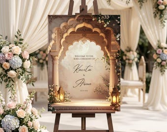 May include: A wooden easel displays a wedding welcome sign. The sign features an ornate arch design with the names "Kavita & Arun" and the date. Lanterns and floral arrangements flank the sign, with the text "Welcome to the Roka Ceremony of".