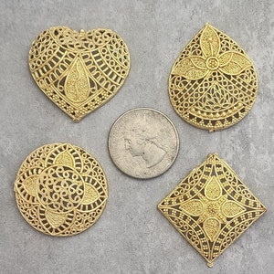 May include: Four gold-colored metal filigree charms in different shapes: a heart, a teardrop, a circle, and a square. The charms have intricate designs and are perfect for jewelry making or crafting.