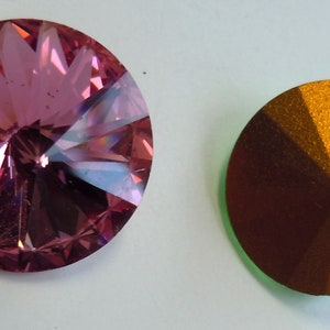 May include: Two round, faceted, decorative buttons. The button on the left is pink and the button on the right is copper.