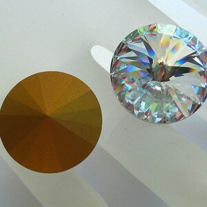 May include: Two round, faceted glass rhinestones. One is clear with rainbow iridescent facets, the other is a gold color.