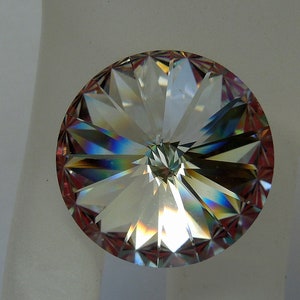 May include: A clear crystal with a faceted design, showing rainbow colors. The crystal is round and has a flat back.