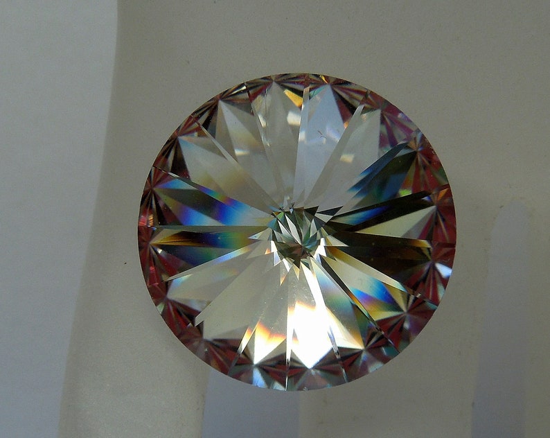 May include: A clear crystal with a faceted design, showing rainbow colors. The crystal is round and has a flat back.