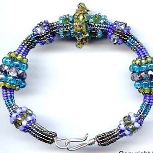 May include: A beaded bracelet with a central design featuring a cluster of purple, green, and clear beads. The bracelet is made with a variety of small beads in shades of purple, green, and clear, creating a textured and intricate look.