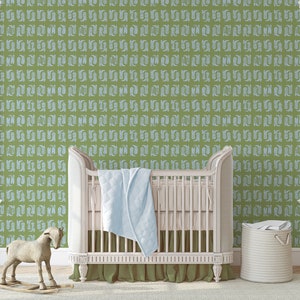 May include: A white crib with a light blue blanket and a white wicker basket in a nursery with green wallpaper featuring a repeating pattern of white stylized leaves.